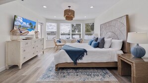 A bedroom with a large bed, a TV, a dresser, and a window with blinds. - 530 Coastal Cabana – Waterfront Pool Home w/ Hot Tub, Dock, Golf Cart & Walk to Beach (Indian Rocks Beach)