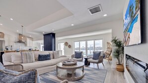 A spacious living room with a large sofa, a coffee table, and wicker chairs. There is a large window with a view of the city. - 530 Coastal Cabana – Waterfront Pool Home w/ Hot Tub, Dock, Golf Cart & Walk to Beach (Indian Rocks Beach)