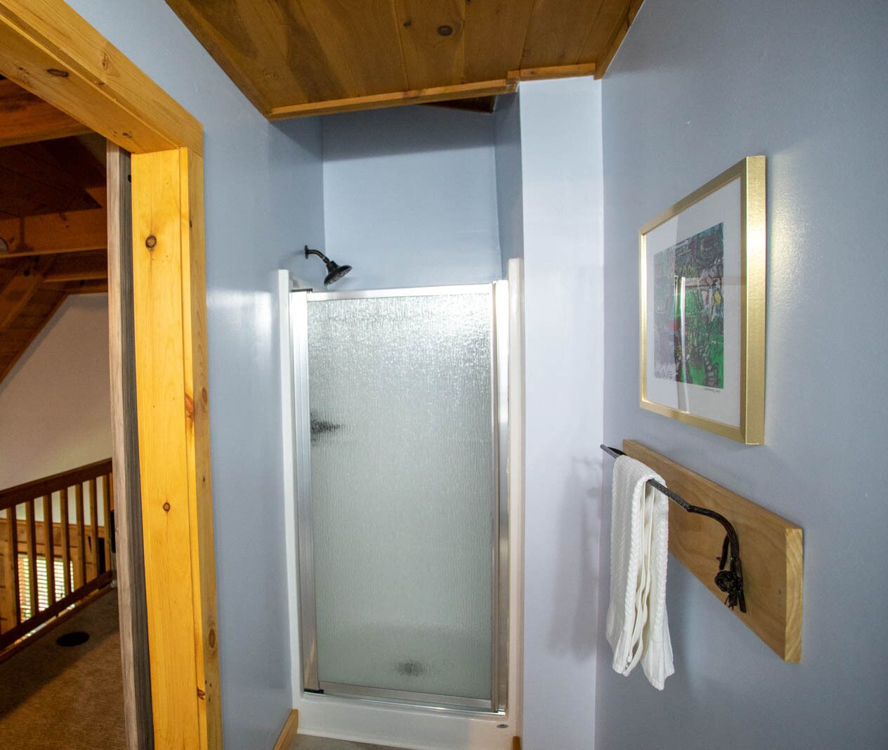 Um chuveiro com portas de vidro jateado, um banco de madeira e um porta-toalhas com uma toalha.