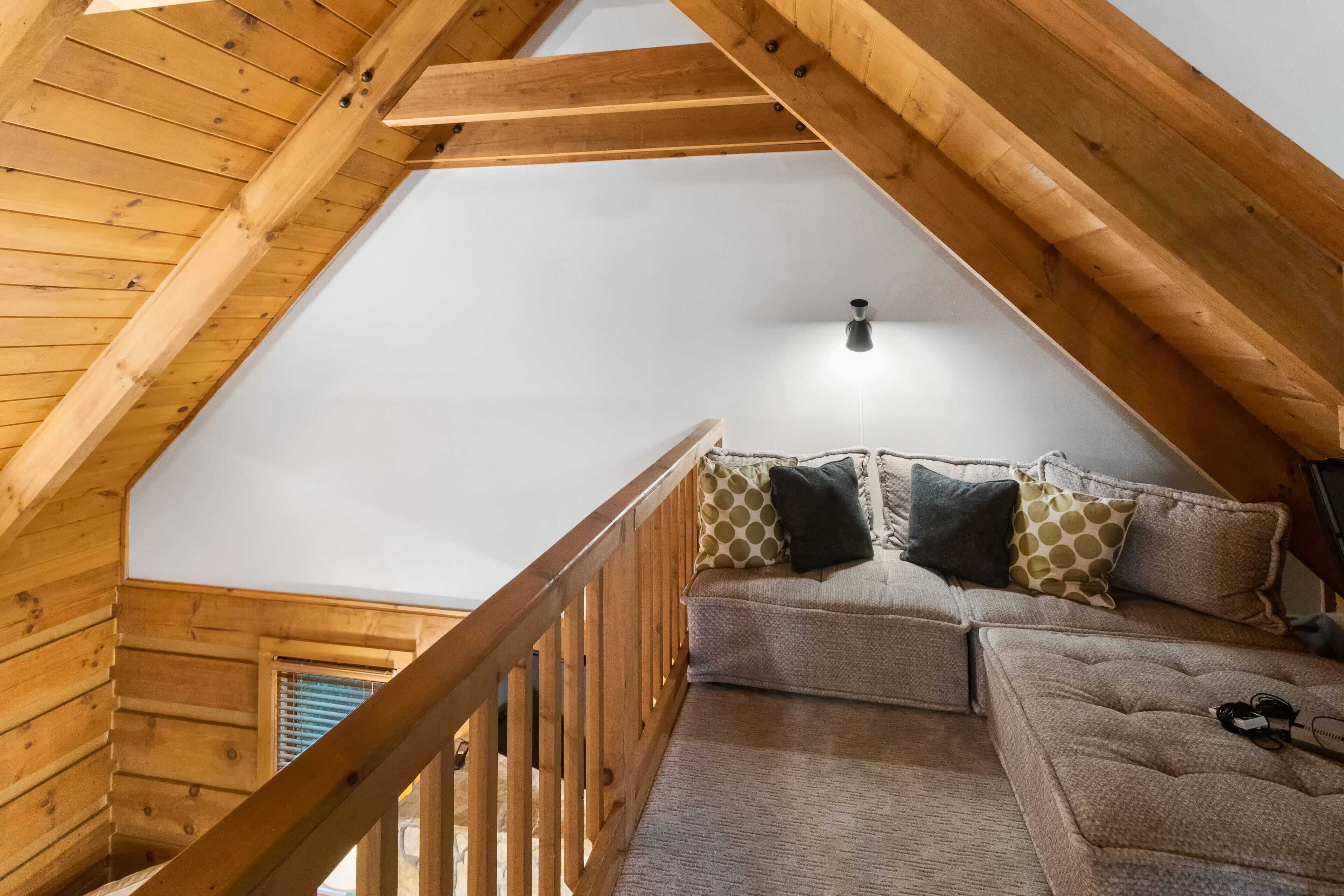 A loft bedroom with a wooden ceiling, a cushioned sofa, and a wooden railing.