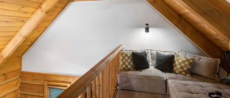 A loft bedroom with a wooden ceiling, a cushioned sofa, and a wooden railing.