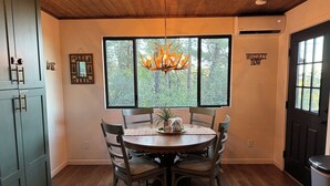 A dining area with a wooden table, four chairs, a chandelier, and a window with a view of trees. - Cozy Cabin in the Pines with Views! (Prescott)