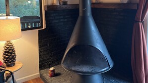 A modern fireplace with a chimney, a window with a view of trees, and a mirror on the wall. - Cozy Cabin in the Pines with Views! (Prescott)