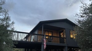 A two-story cabin with a balcony, a stone foundation, and an American flag. - Cozy Cabin in the Pines with Views! (Prescott)