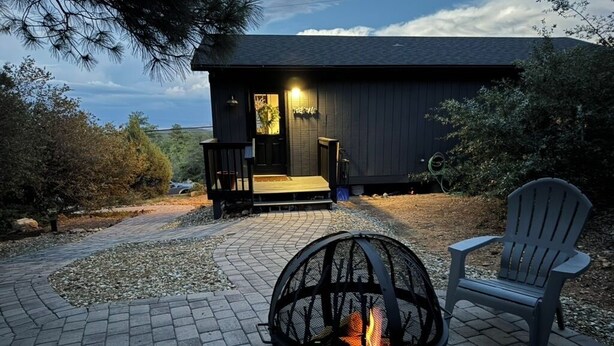 A fire pit in front of a building with a porch and a chair. - Cozy Cabin in the Pines with Views! (Prescott)