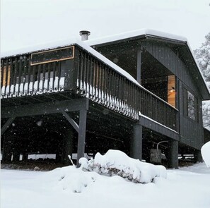 A wooden cabin with a covered porch and a chimney, surrounded by snow. - Cozy Cabin in the Pines with Views! (Prescott)