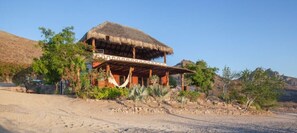 Situated in a natural landscape, this traditional guest house features a simple, open design with a flat roof and wooden beams.