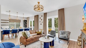 Ein modernes Wohnzimmer mit einem braunen Ledersofa, blauen Sesseln, einem runden Couchtisch und einer Kristallleuchter.