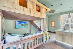 A bunk bed with a wooden exterior, a kitchen area with a sink and cabinets, and a painting of a tropical scene on the wall.