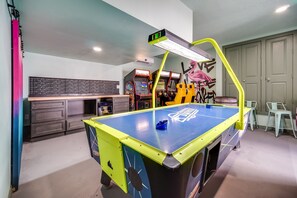 A pool table with a neon light, arcade machines, and a mural on the wall.