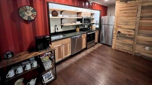 Una cucina con mobili in legno, un frigorifero in acciaio inossidabile e un forno a microonde. Il pavimento è in legno e una parete rossa con un orologio.