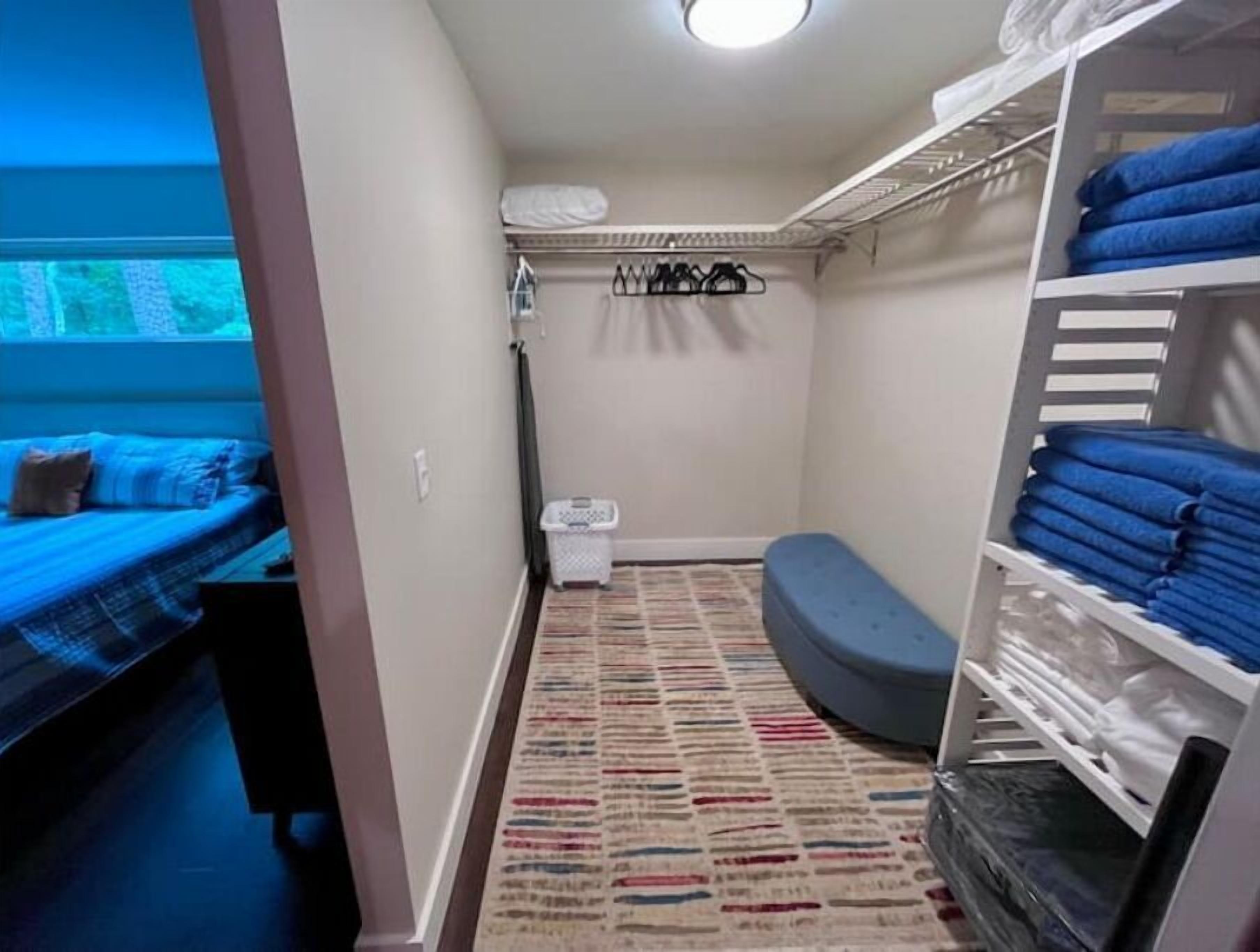 A small, well-organized bedroom with a bed, a bench, a wardrobe, and a window.