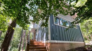 Una baita con una scala in legno che conduce a un ingresso con finestra, immersa tra gli alberi.