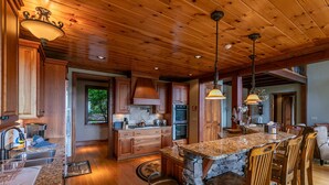 A spacious kitchen with wooden cabinets, granite countertops, and a large island with bar stools. - Haven at Headwaters: Long-range Mountain Views, Pet Friendly, Gameroom (Elk Park)