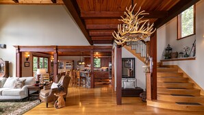 A spacious living room with a wooden staircase, a dining area, and a kitchen. - Haven at Headwaters: Long-range Mountain Views, Pet Friendly, Gameroom (Elk Park)