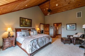 Ein Schlafzimmer mit einem großen Bett, einem Holzkopfende, zwei Nachttischen mit Lampen, einem Deckenventilator und einer Tür zu einem weiteren Raum.