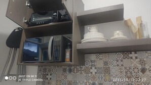 Una cocina con microondas, tostadora y estantes con vajilla y utensilios.