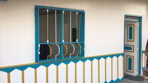 Un edificio con una ventana y una puerta, ambas con detalles azules y amarillos, y una pared blanca con un borde decorativo.