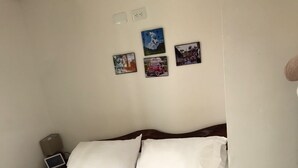 Una cama bien hecha con ropa de cama blanca y aguamarina, una mesita de noche con una lámpara y tres cuadros en la pared.