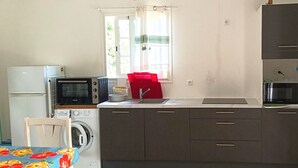 A compact kitchen with a washing machine, microwave, and a red chair.