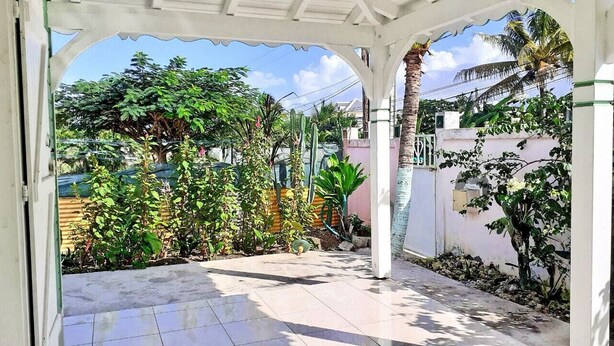 A covered patio area with a tiled floor, surrounded by various plants and a palm tree.
