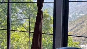 Une pièce dotée d’une grande fenêtre donnant sur un paysage montagneux. On y aperçoit deux chaises et une table au premier plan.