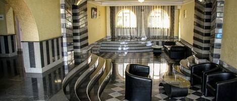 A lobby with a checkered floor, curved seating, and large windows with curtains.