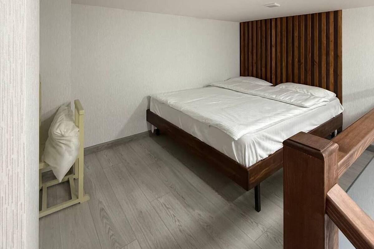 Un dormitorio con estructura de cama de madera, ropa de cama blanca y cabecera de madera.