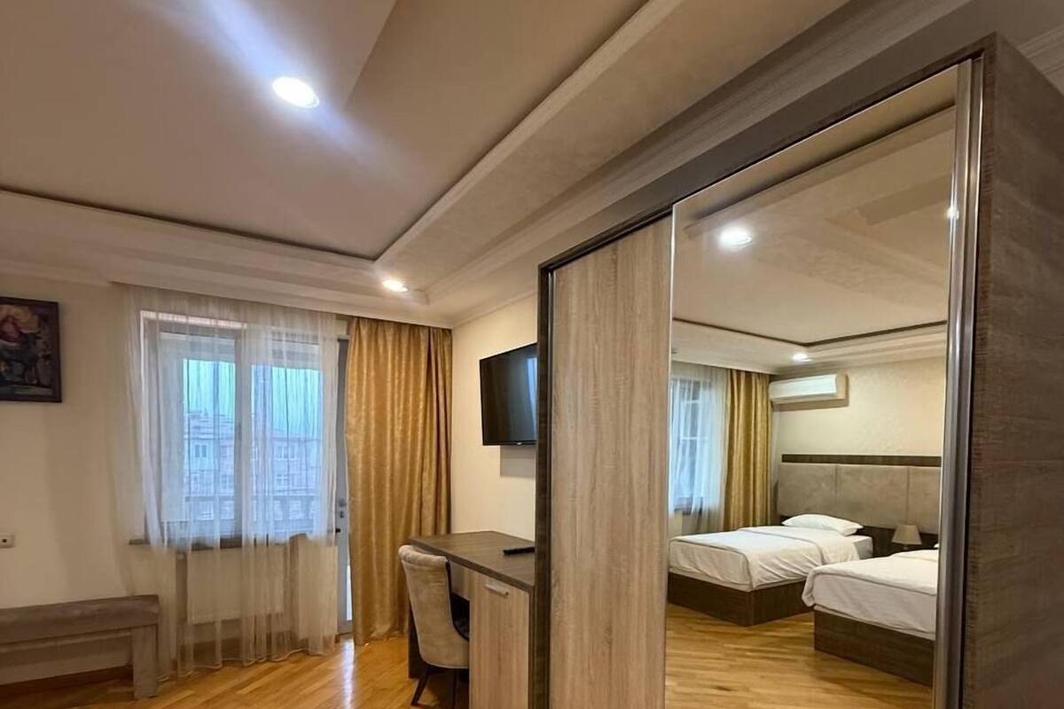 Habitación de hotel con piso de madera, un escritorio con silla, cama con dos almohadas, televisor montado en la pared y un espejo grande.