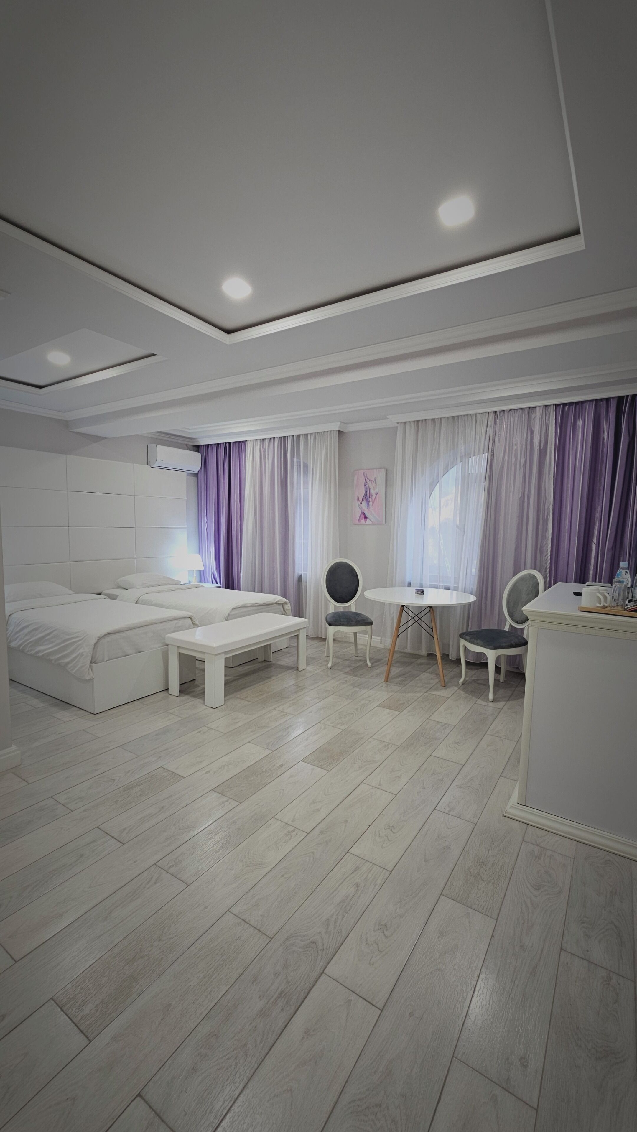 Een moderne hotelkamer met twee bedden, een bureau, stoelen en een groot raam met gordijnen.