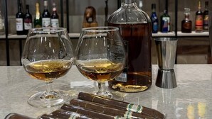 Un coin bar avec deux verres de whisky, une carafe et un shaker à cocktails en métal, le tout posé sur un comptoir en marbre. À l’arrière, des étagères sont remplies de différentes bouteilles de spiritueux.