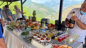 Une table de buffet proposant une variété de fruits, de desserts et de boissons, le tout disposé devant un paysage montagneux.