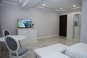 A modern hotel room with a flat-screen TV, a dining table with chairs, a sofa, and a wardrobe.