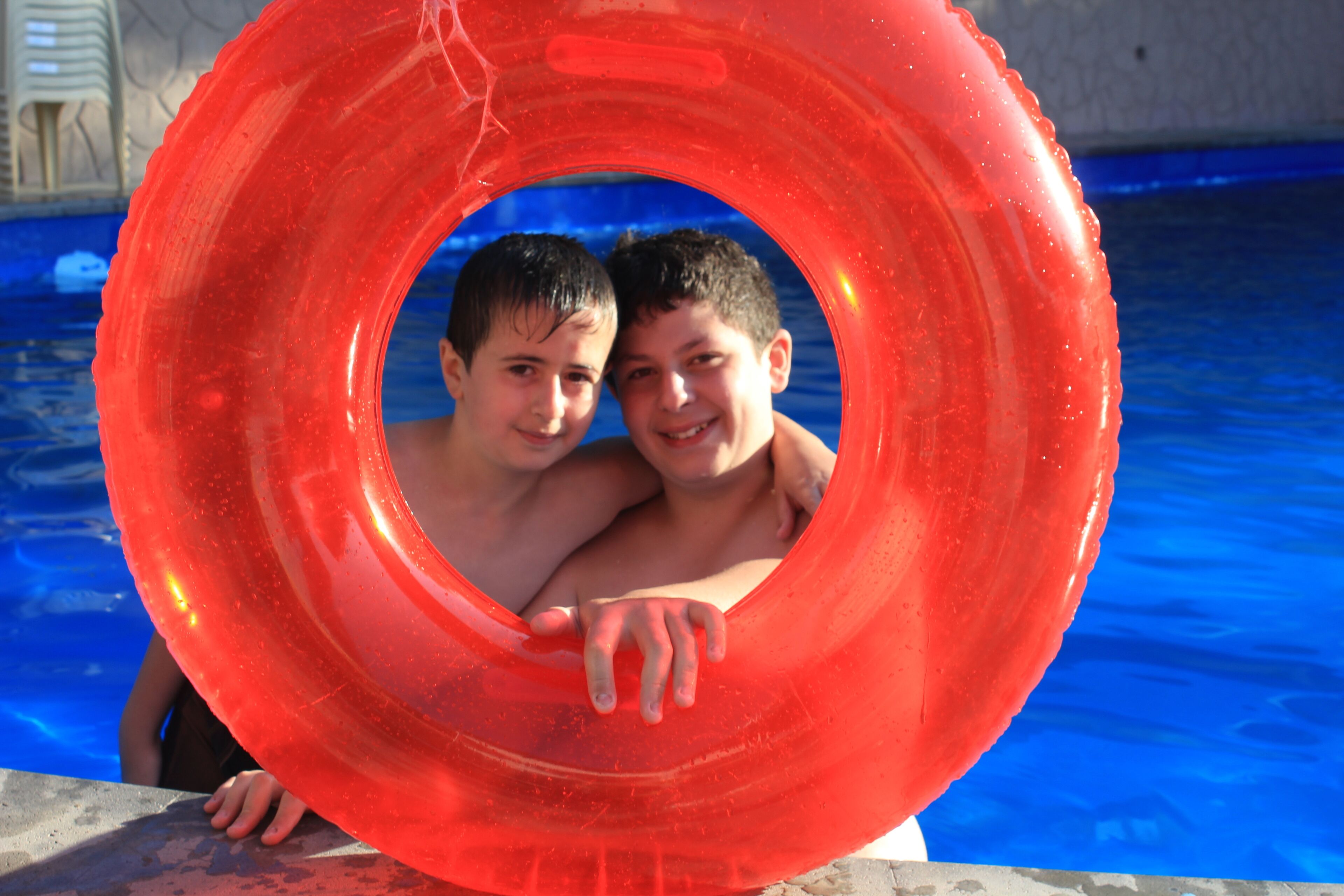 Two people inside a red inflatable ring in a swimming pool.