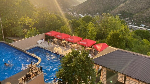 Un espace piscine agrémenté de parasols rouges, avec une vue sur les montagnes et un coucher de soleil.