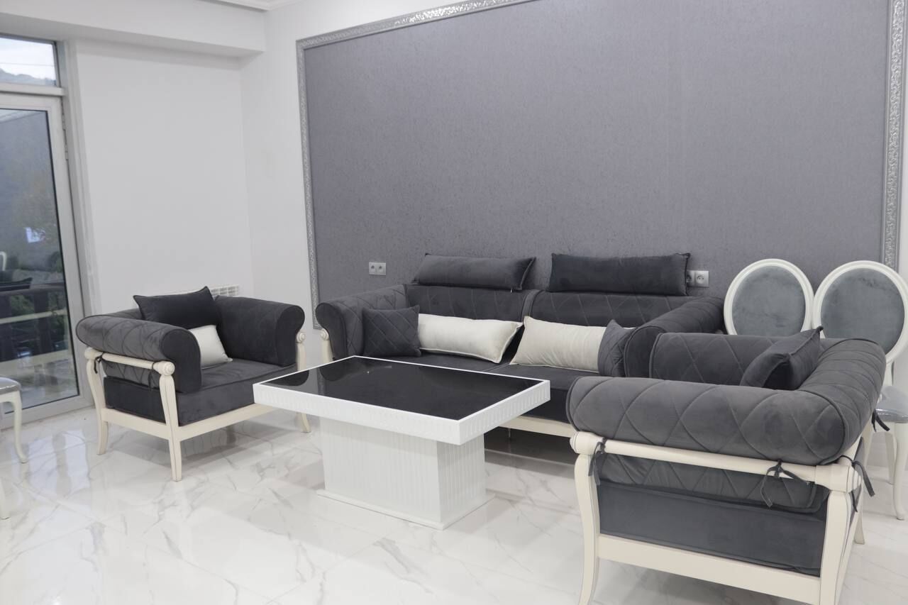 A modern living room with a grey sofa set, a white coffee table, and a large window providing natural light.