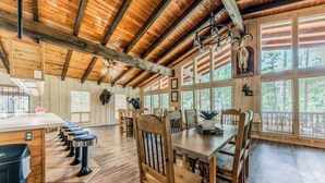 A wooden interior with a dining area, bar stools, and large windows. - Hidden Buffalo Lodge | Sleeps 13 w/Kid's Loft! (Alto)