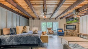 A spacious bedroom with a large bed, a seating area with a sofa and chairs, a fireplace, and a television mounted on the wall. - Hidden Buffalo Lodge | Sleeps 13 w/Kid's Loft! (Alto)