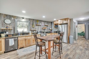 Een moderne keuken met houten kastjes, een groot eiland met barstoelen, roestvrijstalen apparatuur en een rustieke wandafwerking.