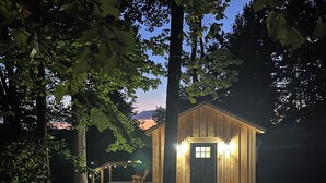 Una cabaña de madera con un porche, rodeada de árboles.