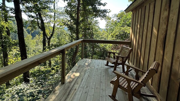 Una terraza de madera con barandilla, bancos y vista a un área boscosa.
