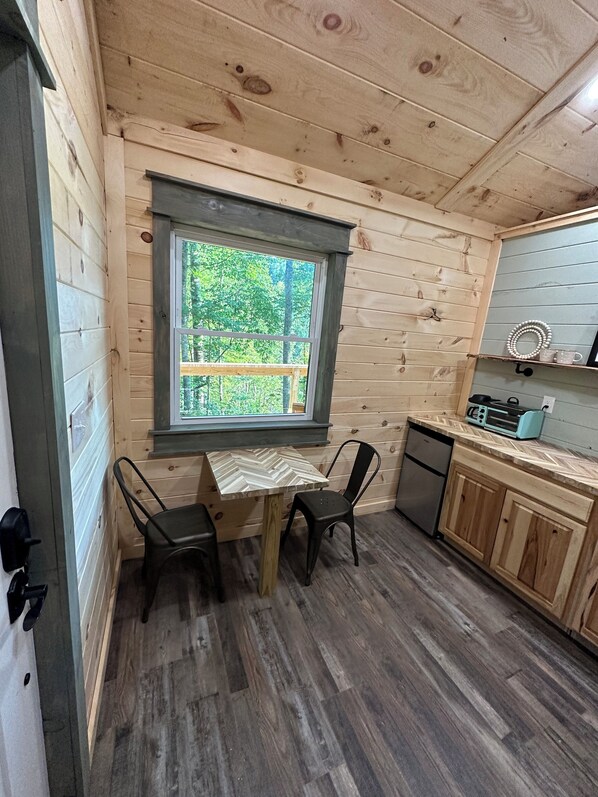 A compact kitchen with wooden walls, a herringbone-patterned table, two chairs, a toaster, and a dishwasher. - Cabin in the woods (London)