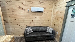 Una habitación acogedora con techo de madera, un sofá de cuero negro con cojines estampados y un equipo de aire acondicionado integrado.