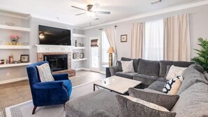 Ein Wohnzimmer mit Kamin, blauem Sessel, grauem Sofa und Deckenventilator.