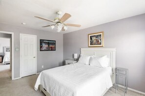 A bedroom with a bed, a ceiling fan, a nightstand, a framed picture, and a door.