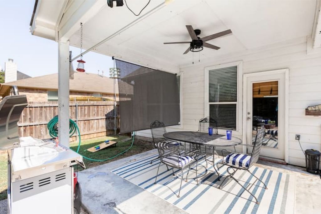 Eine überdachte Terrasse mit Tisch, Stühlen, Deckenventilator und Grill.