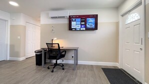 Ein sauberes, modernes Zimmer mit Schreibtisch, Stuhl und einem montierten Fernseher, der verschiedene Sender anzeigt.