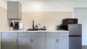 Eine moderne Küche mit grauen Schränken, einer Granit Arbeitsplatte, einer Kaffeemaschine, einer Mikrowelle und einem Kühlschrank.