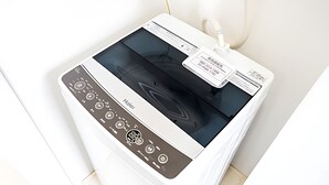 A modern, white, wall-mounted washer and dryer unit with a digital control panel and a label with contact information.