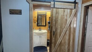 A rustic bathroom with a wooden door, a sink, and a mirror. - Deer Run Cabin (Licking)